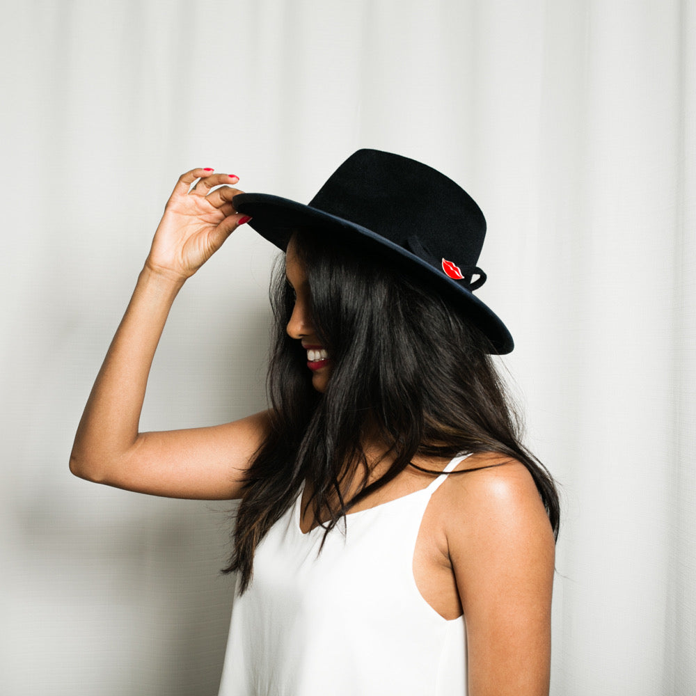 Woman wearing a blue hat with a red lips pin against a white background