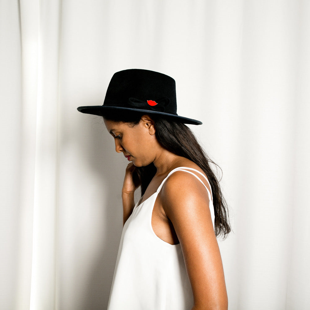 Woman wearing a blue hat with a red lips detail against a white curtain background