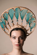 Woman wearing a decorative headpiece with teal leaves and gold frame on a beige background
