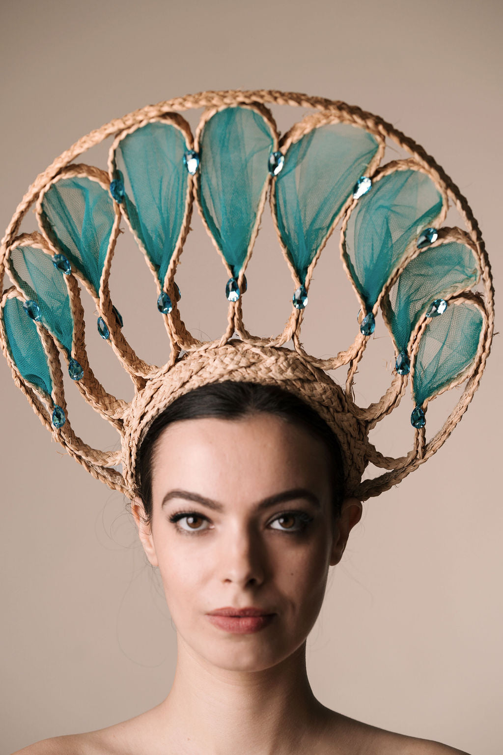 Woman wearing a decorative headpiece with teal leaves and gold frame on a beige background