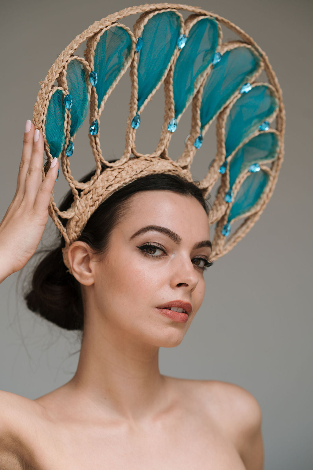 Woman wearing a decorative headpiece with teal feathers against a gray background