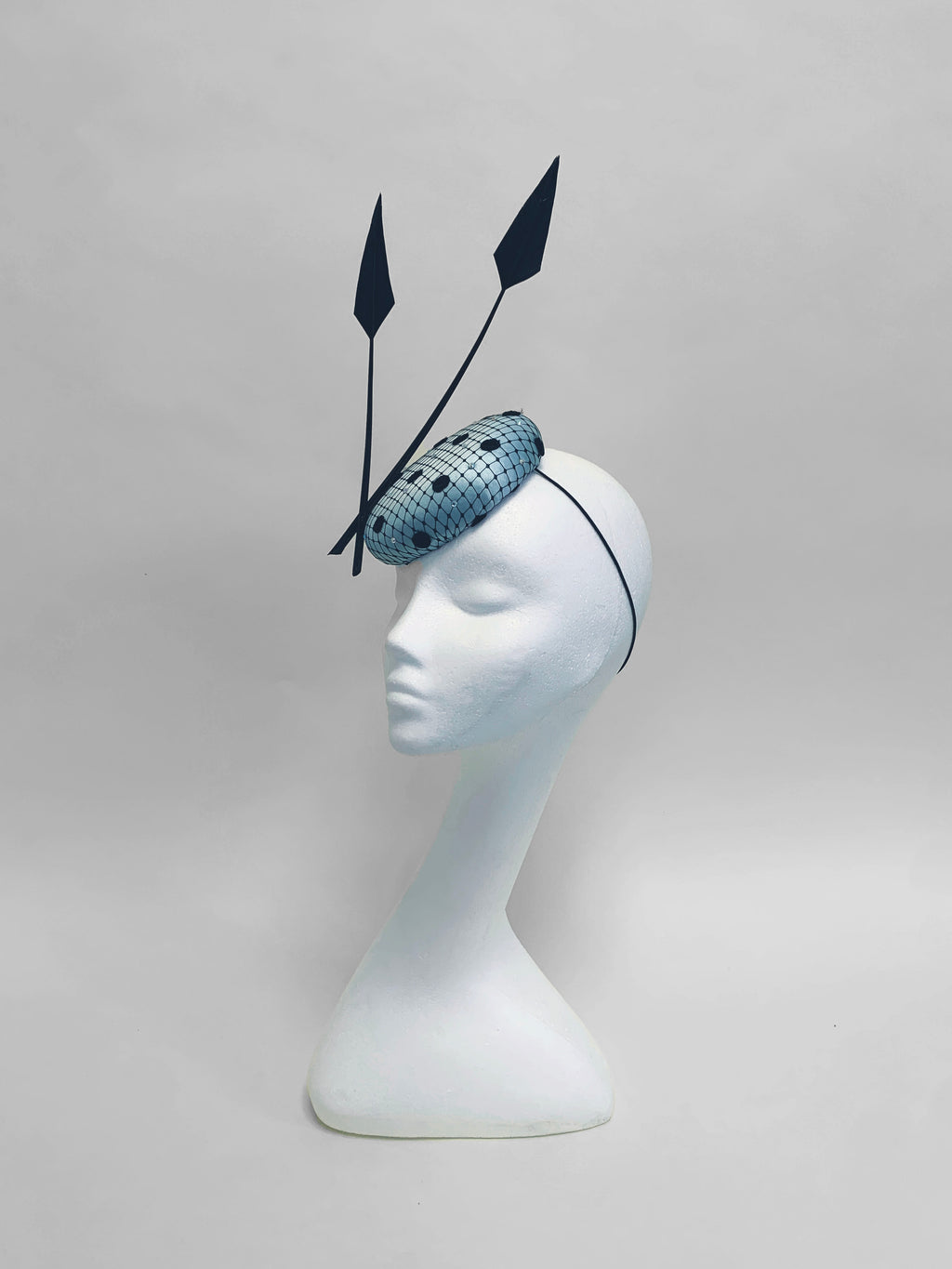 Spherical blue headpiece with black feathers on a white mannequin head against a gray background