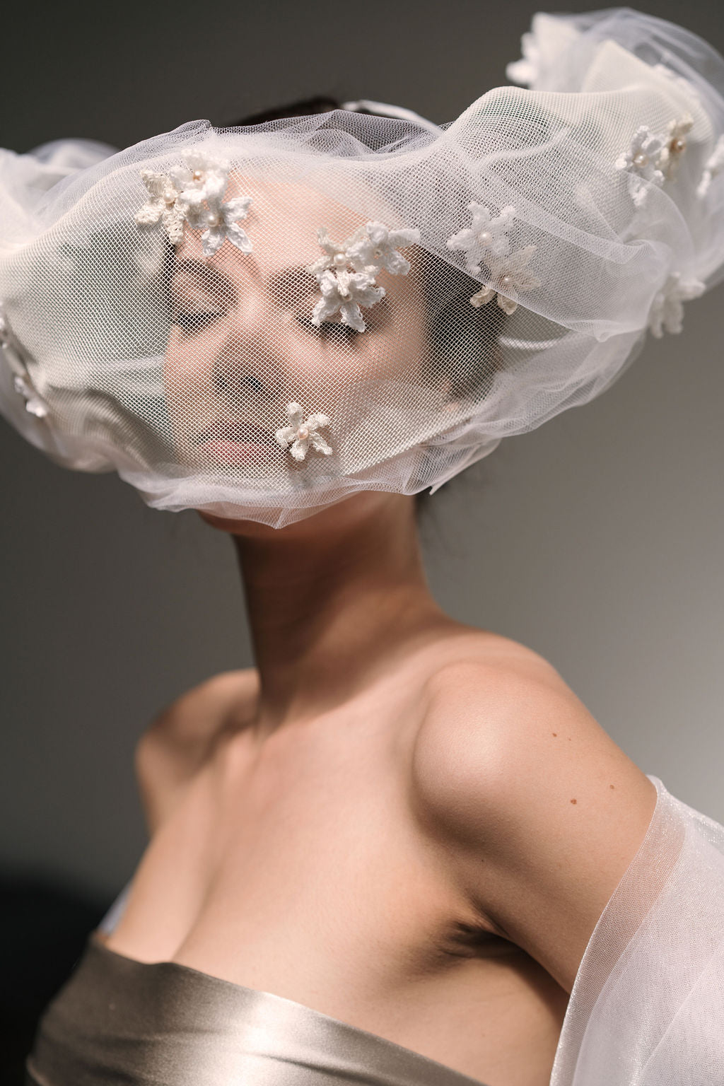 Person wearing a white veil with floral embellishments on a dark background