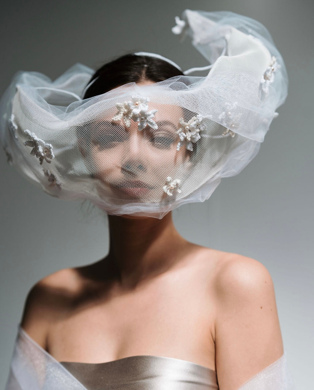 Woman wearing a white veil with floral embellishments on a gray background