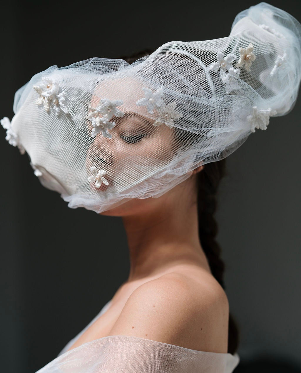 Woman wearing a delicate white veil with floral embellishments against a dark background
