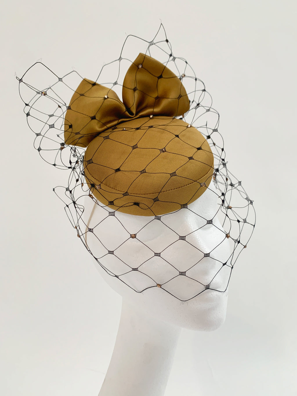 Gold fascinator hat with a netting design on a mannequin head against a white background