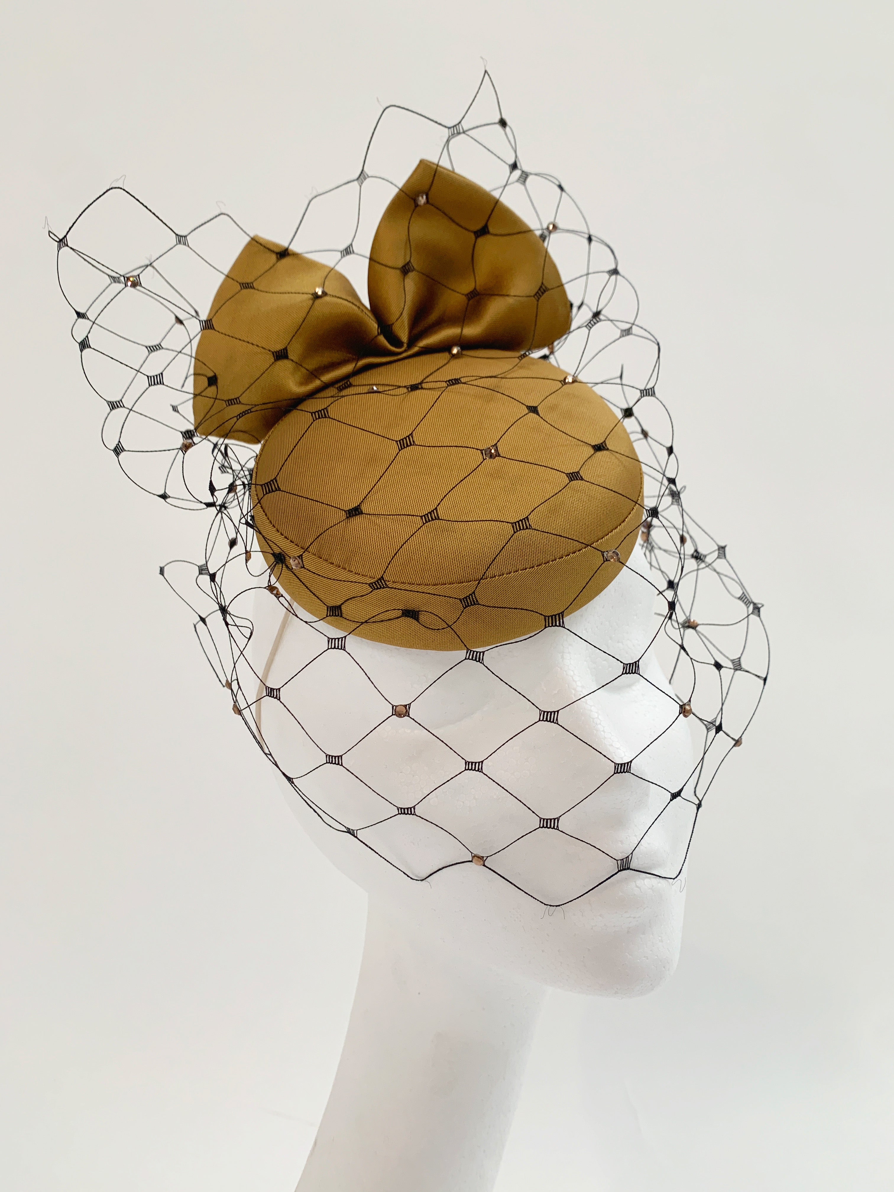Gold fascinator hat with a netting design on a mannequin head against a white background