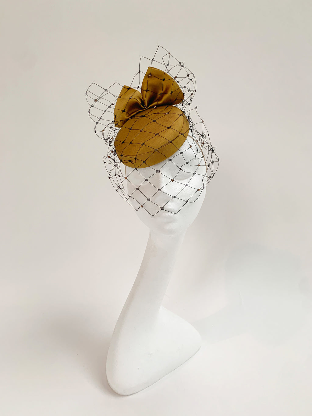 Gold fascinator with a veil on a white mannequin head against a white background