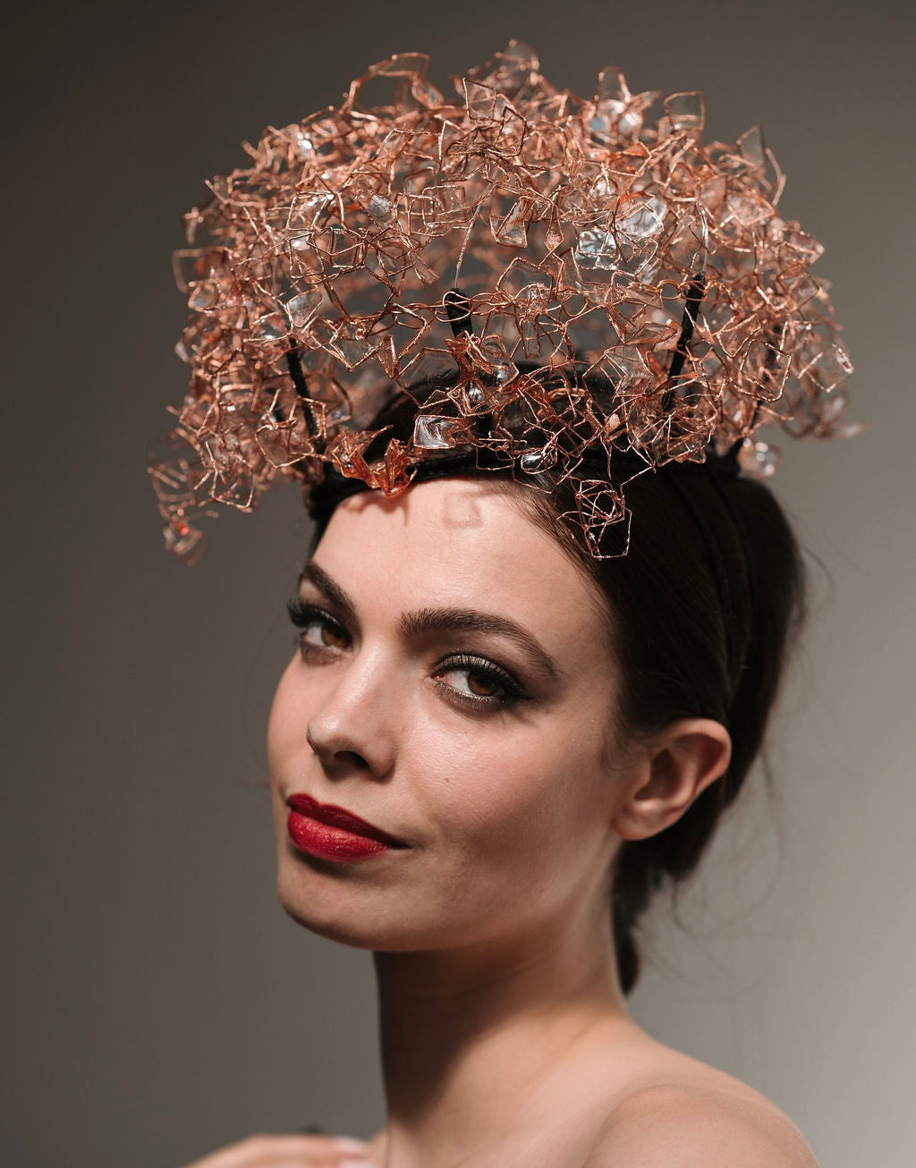 Woman wearing a decorative headpiece with intricate design on a plain background