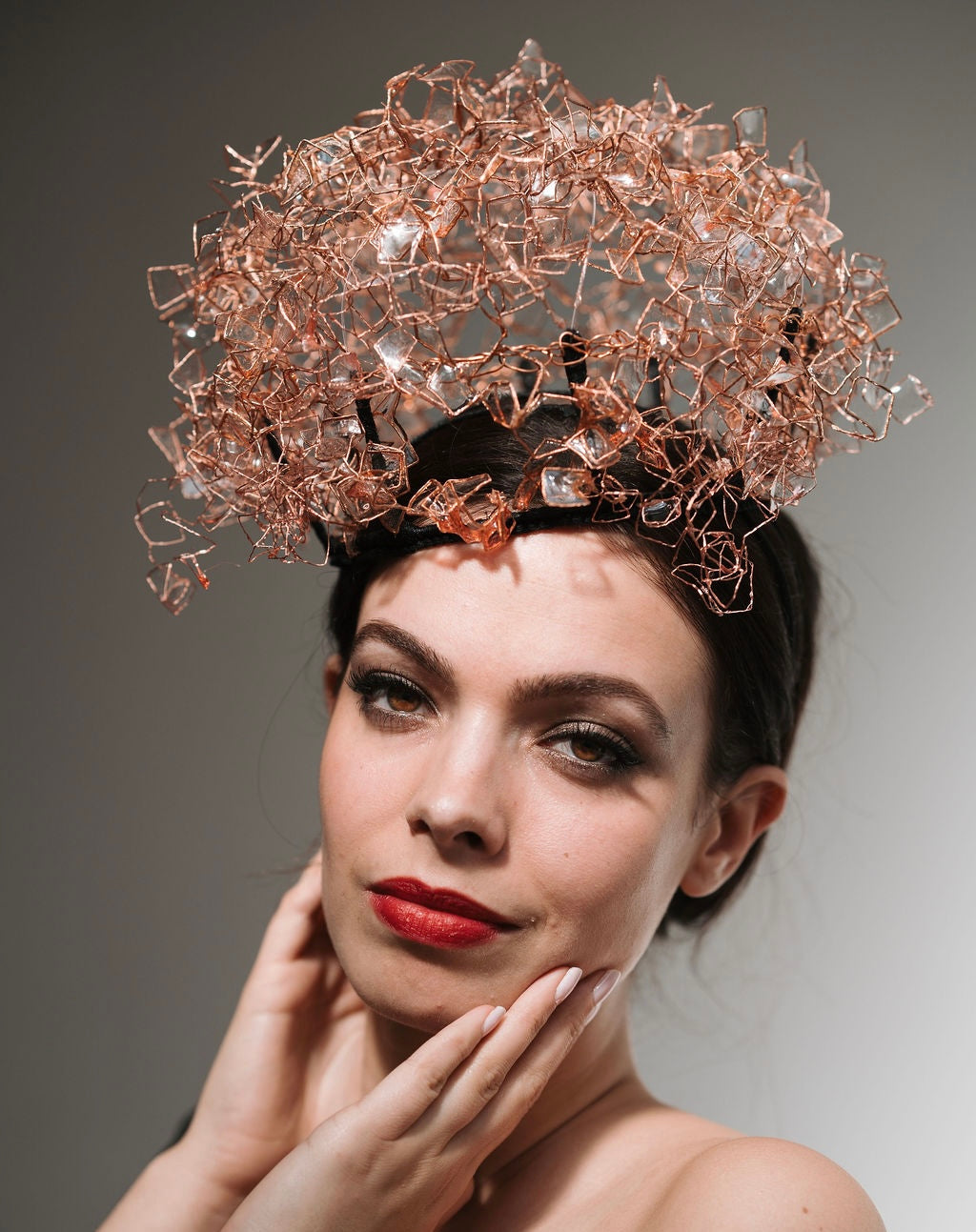 Woman wearing a large, intricate headpiece against a neutral background