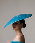 Woman wearing a large blue hat with a gray background