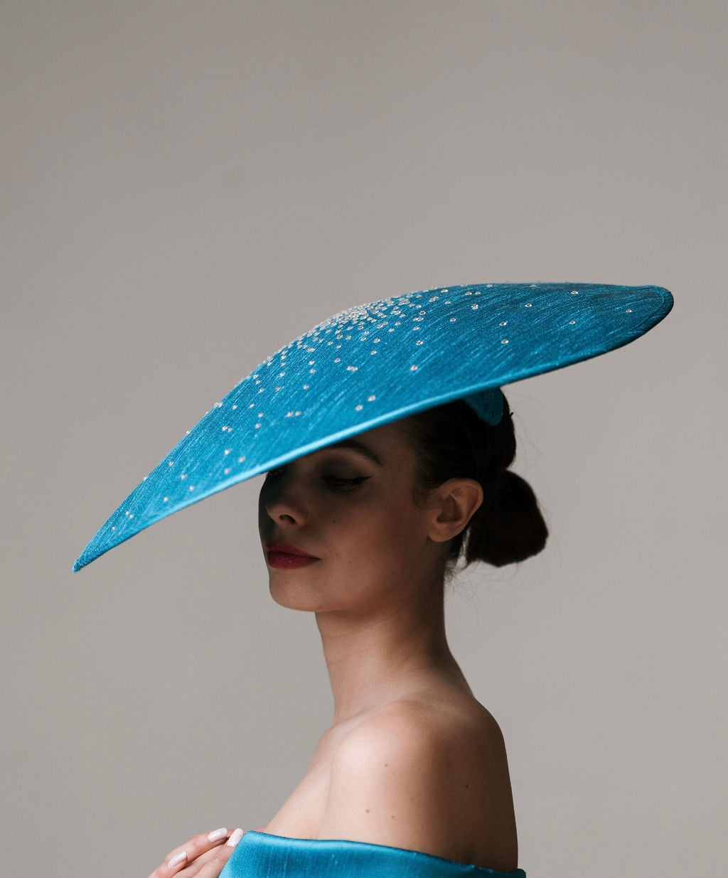 Woman wearing a large blue hat with a gray background