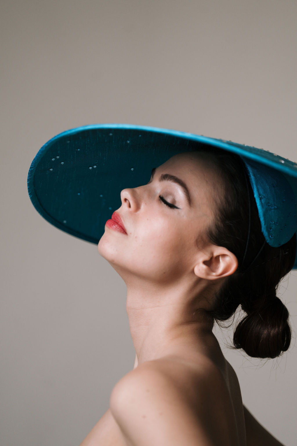 Woman wearing a wide-brim blue  hat against a neutral background