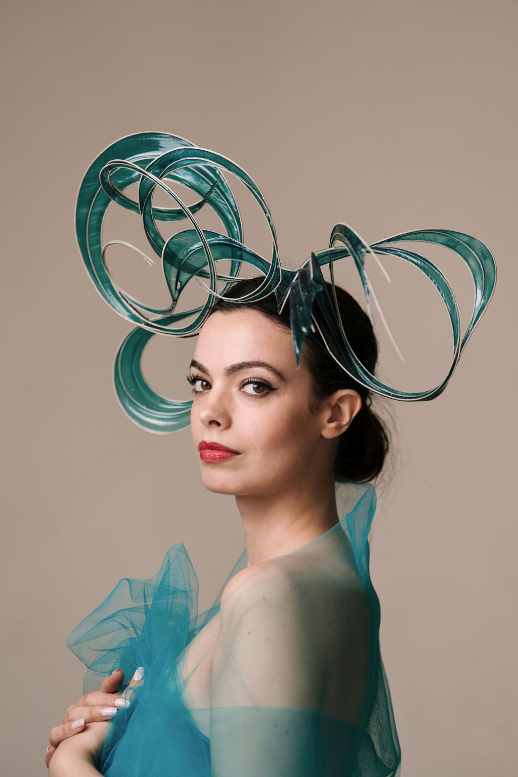 Woman wearing a teal dress with a large, intricate headpiece against a beige background